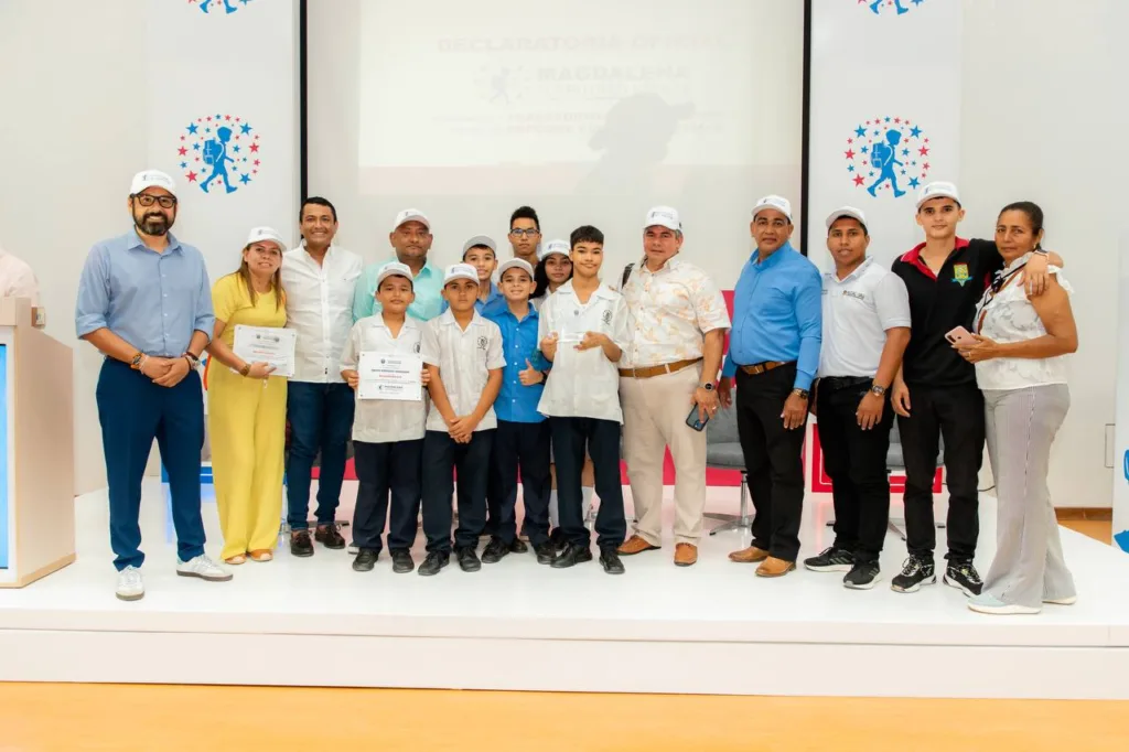 Grupo de estudiantes, docentes y funcionarios de la Secretaría de Educación del Magdalena posan en el escenario durante el evento de celebración del primer año del Magdalena como Territorio STEM+E. Varias personas sostienen certificados y trofeos de reconocimiento.
