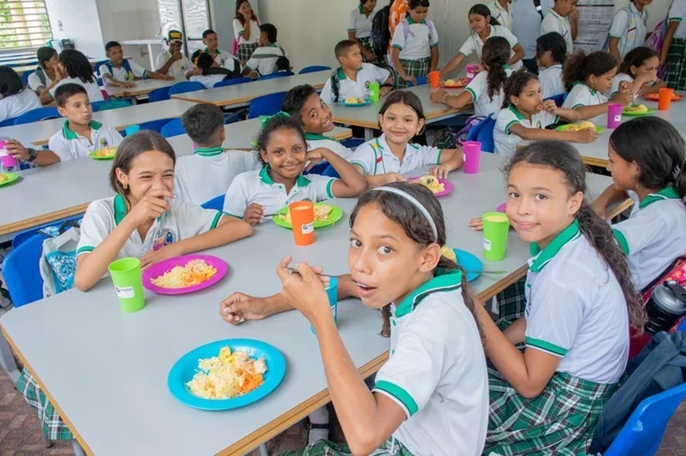 Niñas estudiantes de un colegio sentadas frente a un plato de comida, almorzando