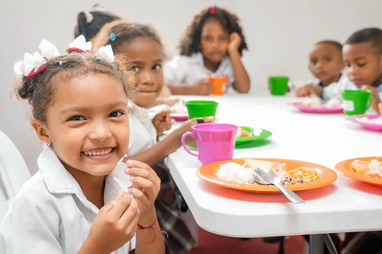 Niñas y niños estudiantes del Magdalena sentados en una mesa disfrutando su almuerzo