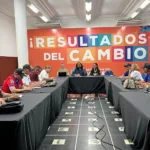 Reunión entre directivos de la Secretaría de Educación y representantes sindicales, sentados en mesas dispuestas en forma de ‘U’, en un salón con un gran mural al fondo que dice ‘¡Resultados del Cambio!’