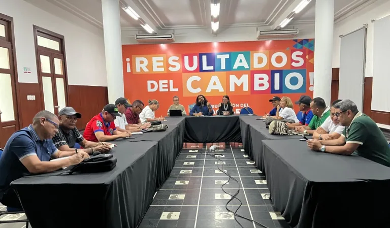 Reunión entre directivos de la Secretaría de Educación y representantes sindicales, sentados en mesas dispuestas en forma de ‘U’, en un salón con un gran mural al fondo que dice ‘¡Resultados del Cambio!’
